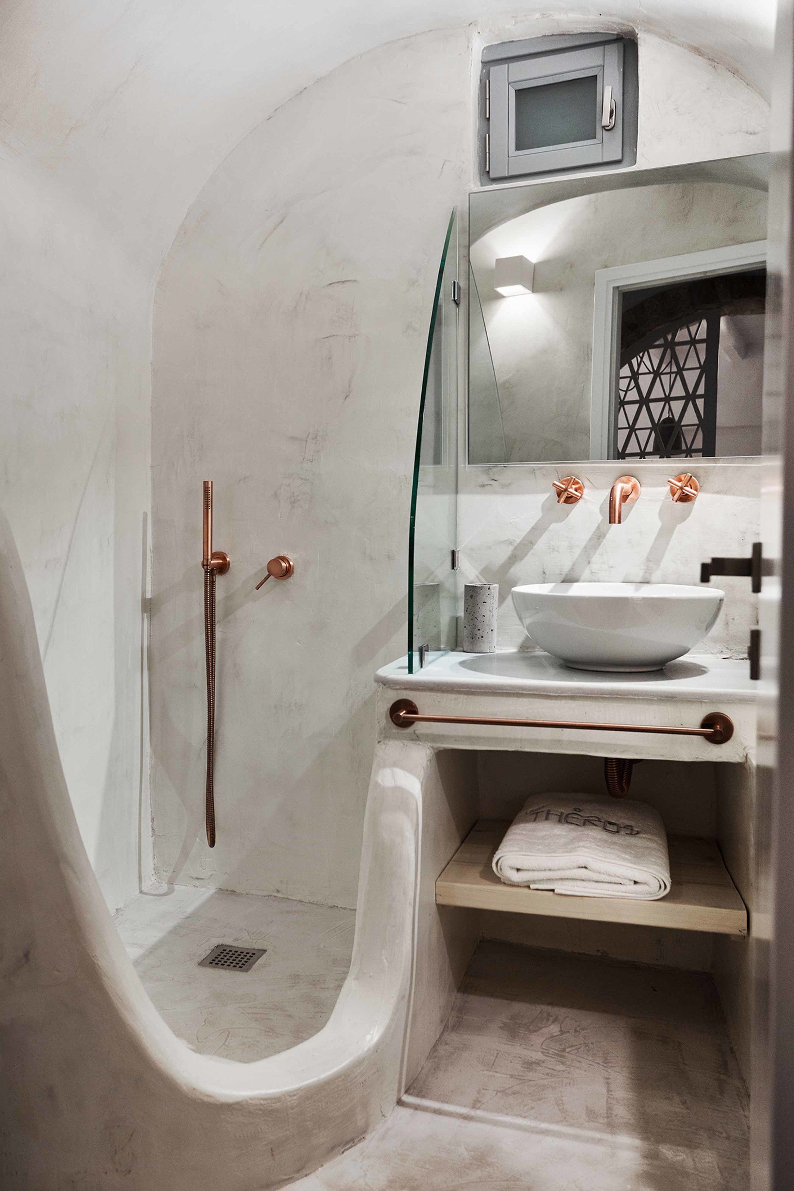 Un baño con cabina de ducha de vidrio, un lavamanos blanco con accesorios de cobre y una pequeña repisa con una toalla.