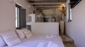 A bedroom with a large bed, a stone wall, a small bathroom, and a window.