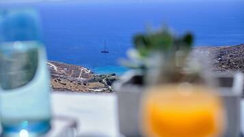 Una mesa con vista despejada al mar y un velero distante, con un paisaje montañoso al fondo.