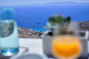 Una mesa con vista despejada al mar y un velero distante, con un paisaje montañoso al fondo.