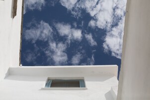 Un edificio blanco con una ventana pequeña y un cielo azul despejado con nubes.