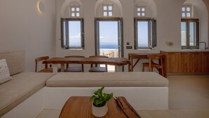En modern inredning med ett matområde, en soffa och utsikt över havet genom välvda fönster.