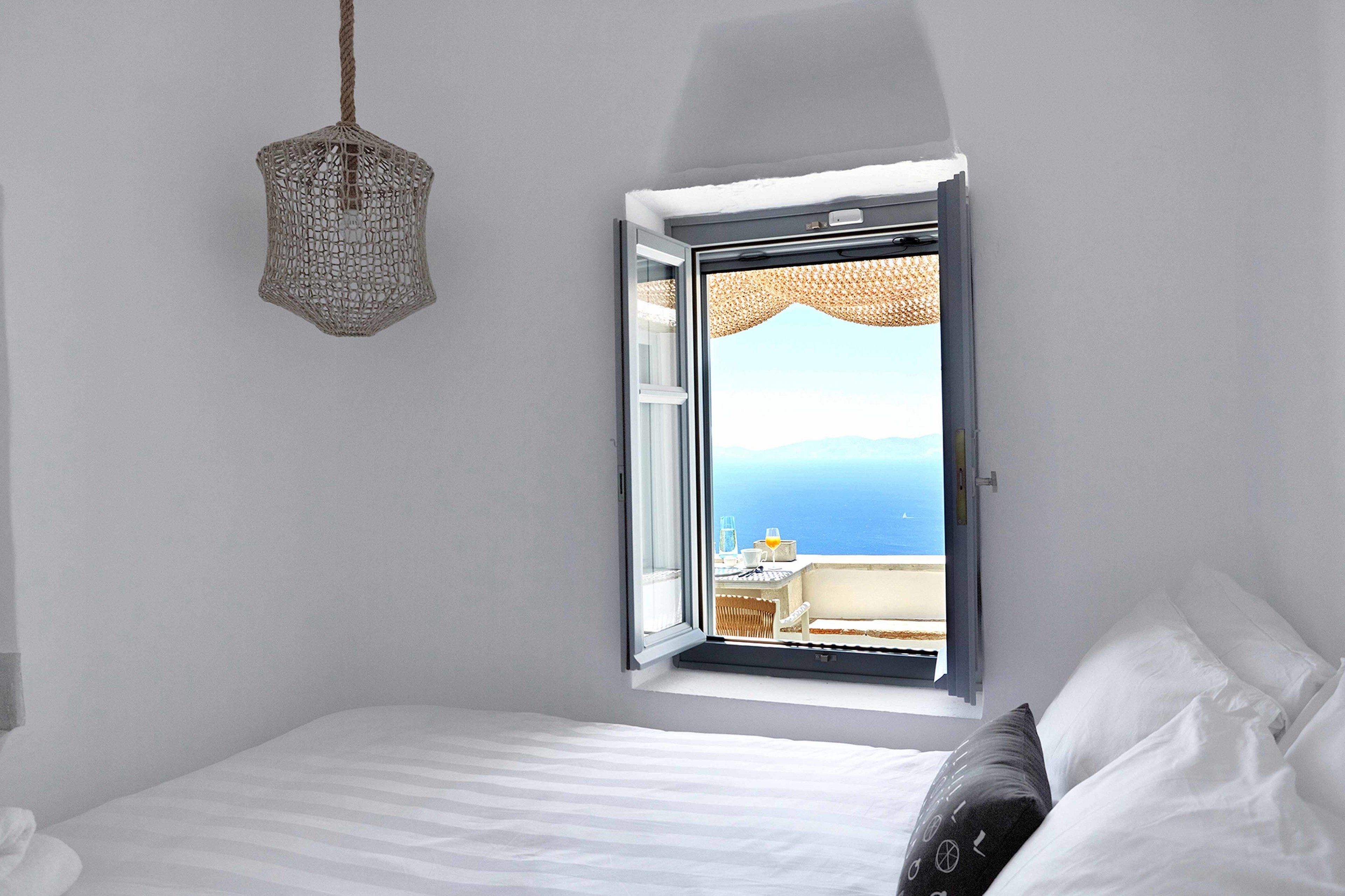 Une chambre à coucher avec un lit, un luminaire suspendu et une fenêtre donnant sur la mer.