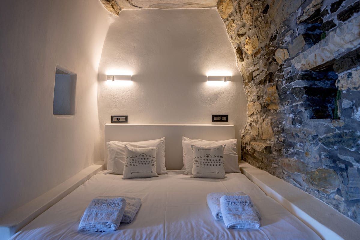 Een slaapkamer met een stenen muur, twee bedden met witte lakens en twee wandlampen.