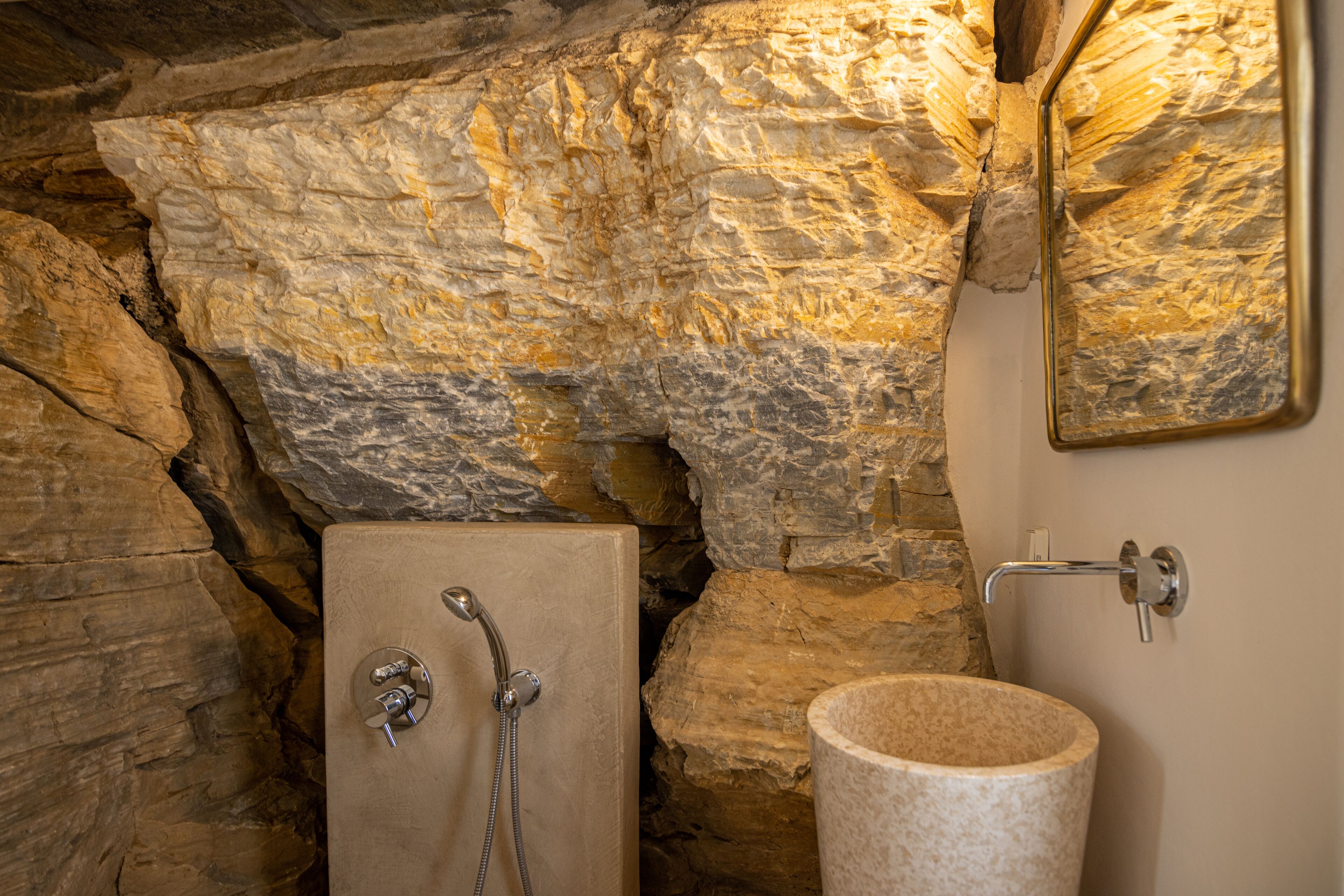 A bathroom with a stone wall, a bathtub, and a sink with a stone basin.