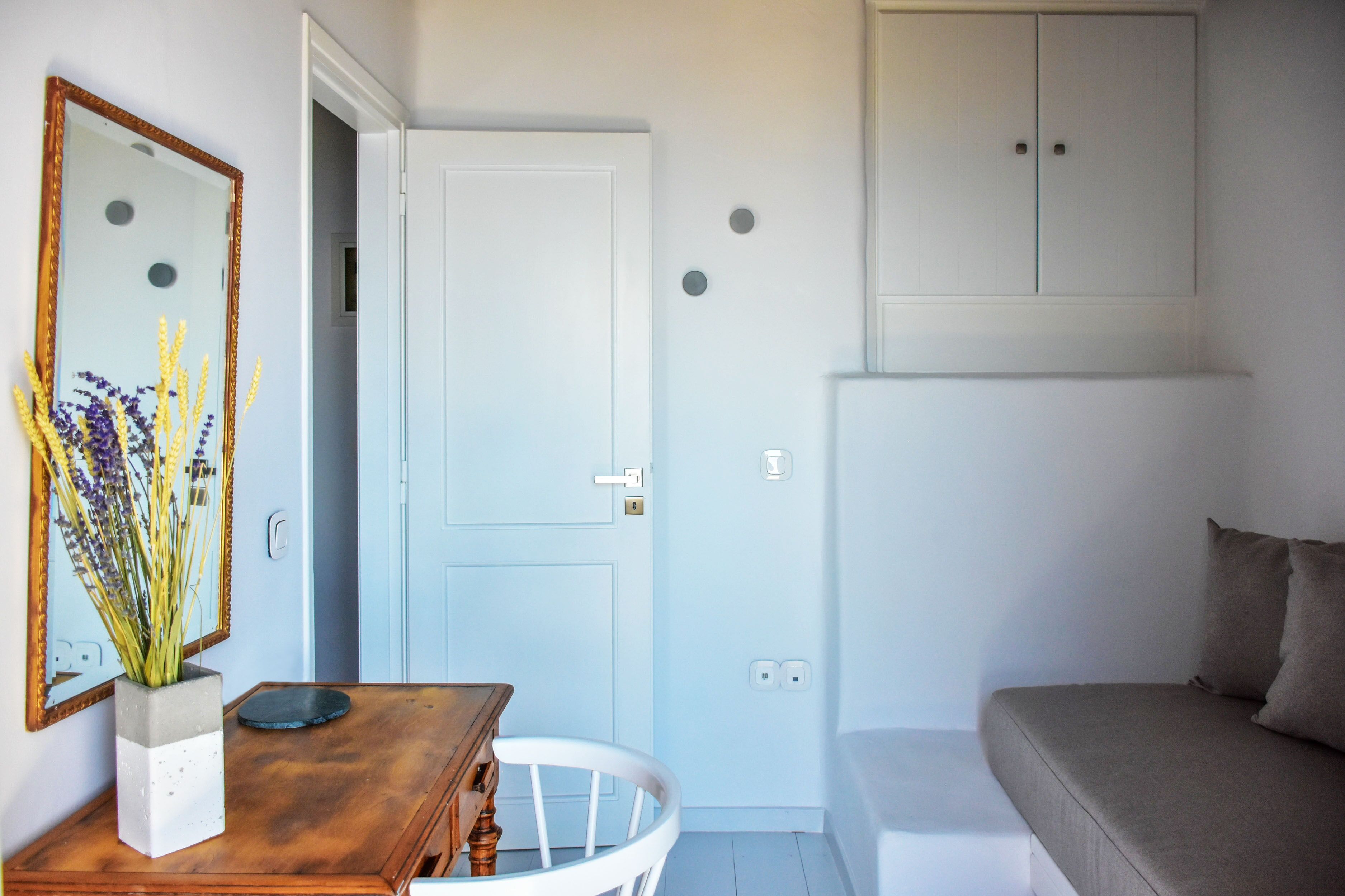 A room with a white door, a wooden table with a vase of flowers, a white chair, and a grey sofa.