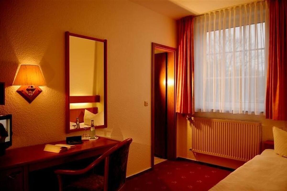 A hotel room with a desk, chair, bed, and a large window with curtains.