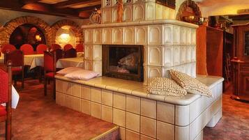 Ein gemütliches Restaurant mit Kamin, rot gepolsterten Stühlen und einem steinernen Bogen.