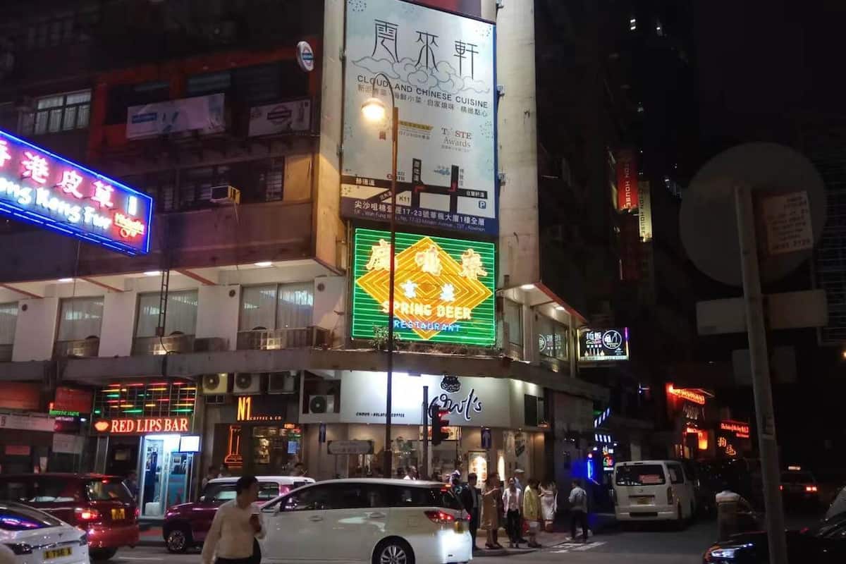 A nighttime street scene with illuminated signs for restaurants and a cloud-themed advertisement.