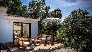 Un patio con mobiliario de madera, una sombrilla blanca y vista a árboles.