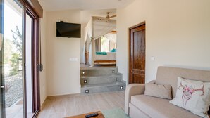 Una sala de estar con un sofá, un televisor montado en la pared y una escalera que lleva a un dormitorio.