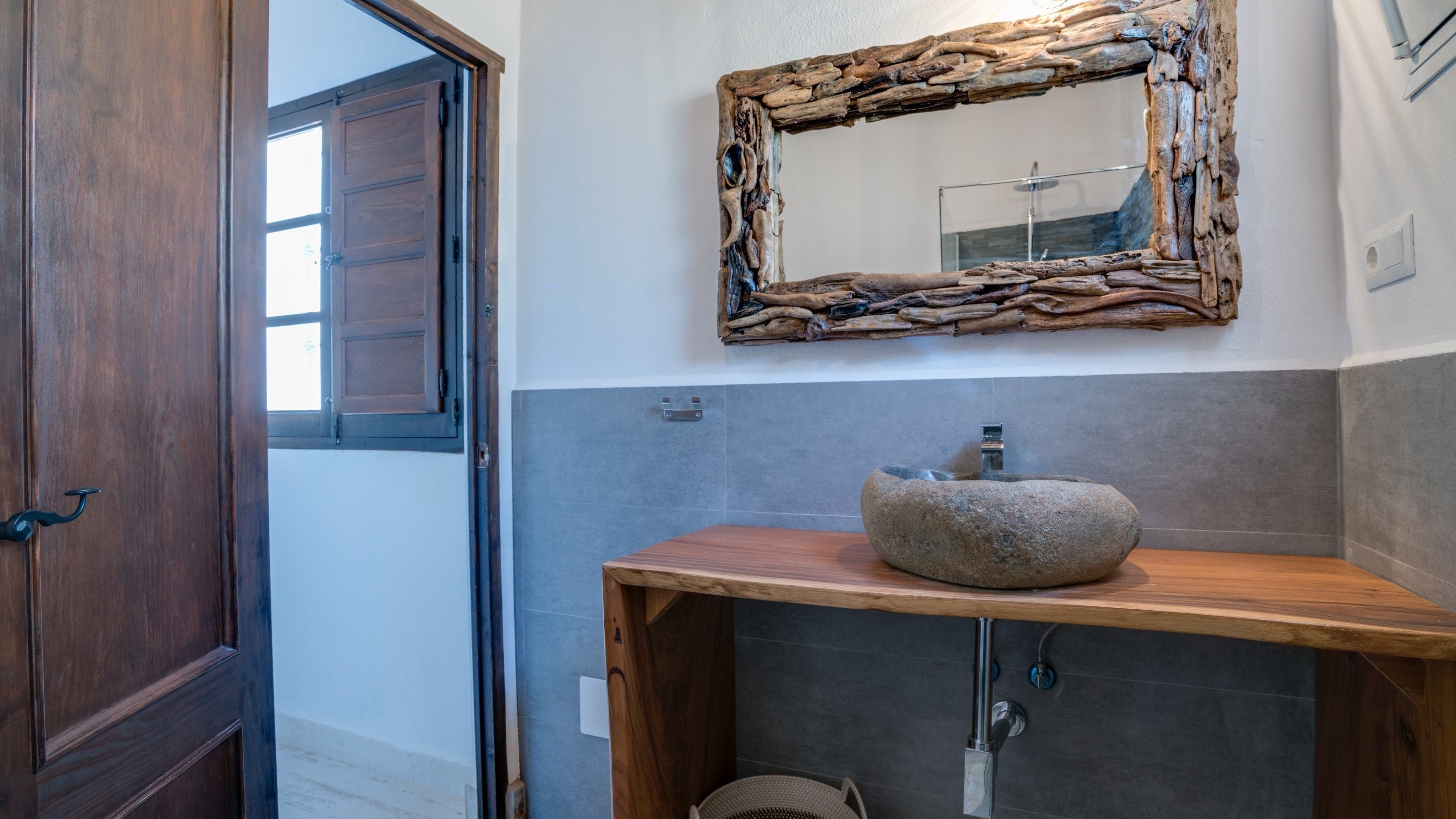 Une salle de bain avec une porte en bois, un lavabo en pierre et un miroir doté d’un cadre rustique.