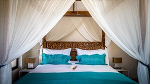 Una cama con cabecera de madera, ropa de cama blanca y azul turquesa, y un dosel blanco.