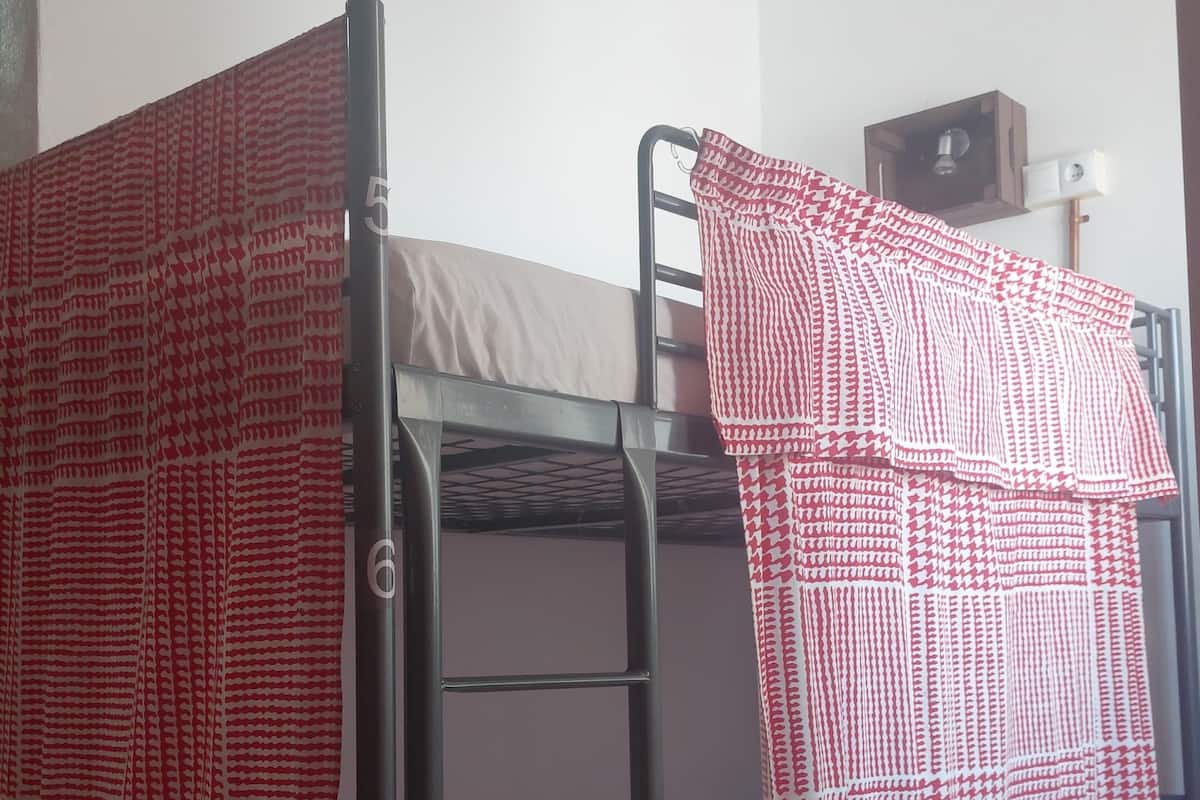 Two bunk beds with red and white patterned bedding, a tiled floor, and a small wooden shelf with a lamp.