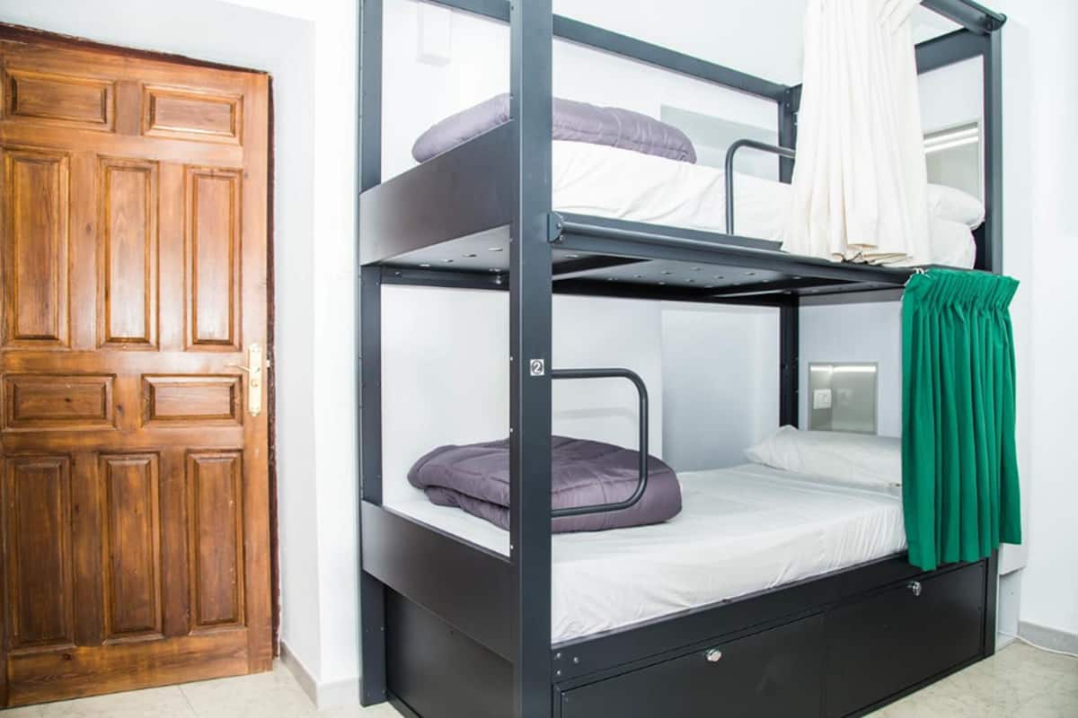 A bunk bed with a green curtain, a wooden door, and a white wall.