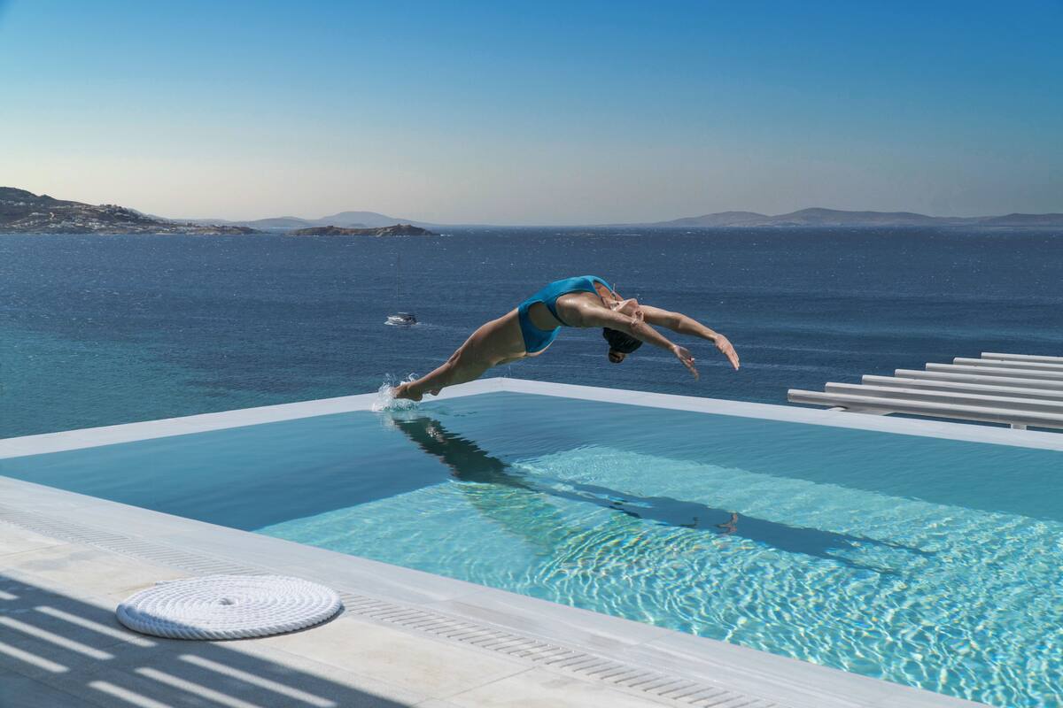 A clear view of a swimming pool with a person diving into the water, surrounded by a poolside area with lounge chairs.
