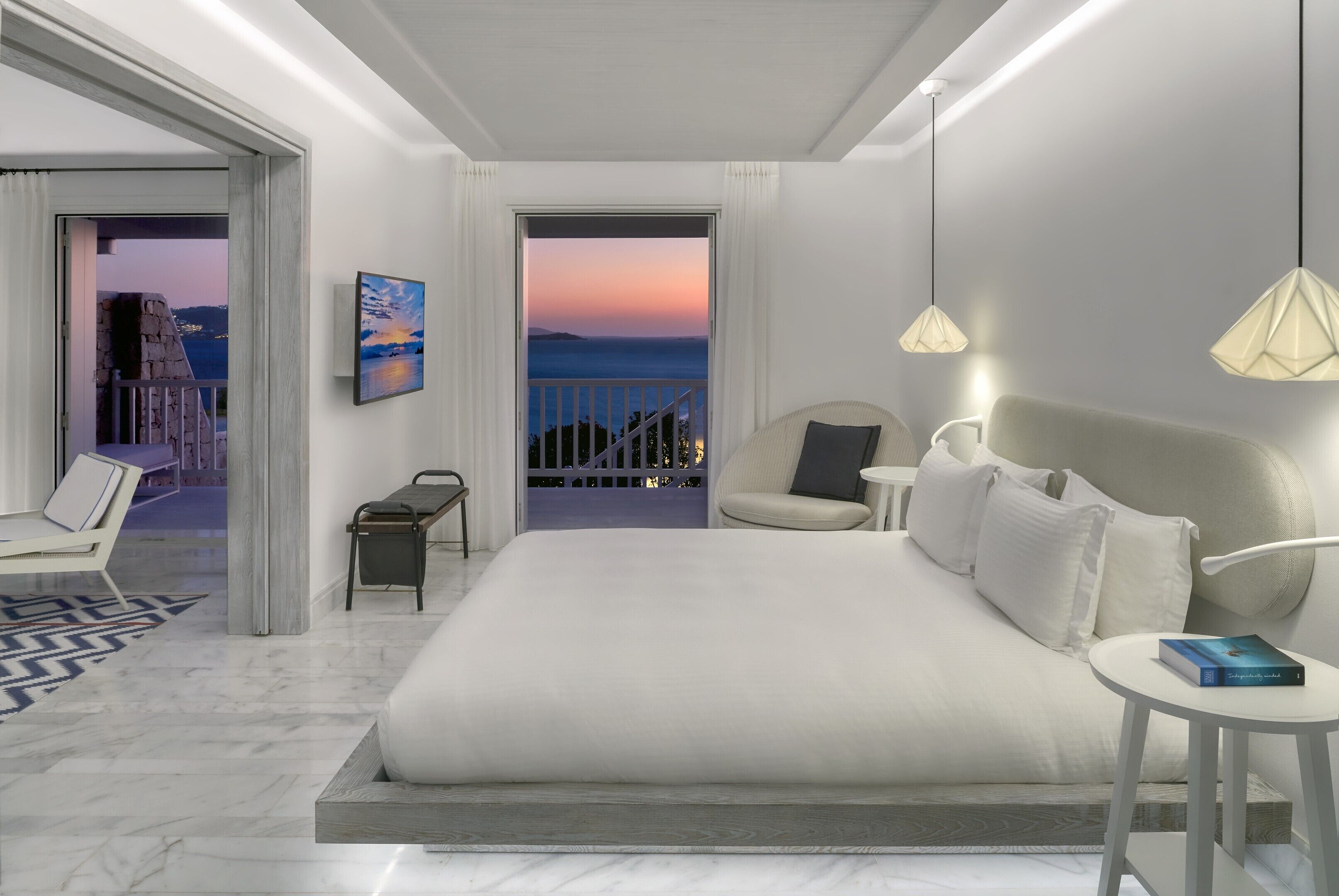 A modern hotel room with a large bed, a view of the sea, a balcony, and a painting on the wall.