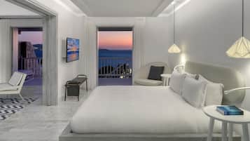 A modern hotel room with a large bed, a view of the sea, a balcony, and a painting on the wall.