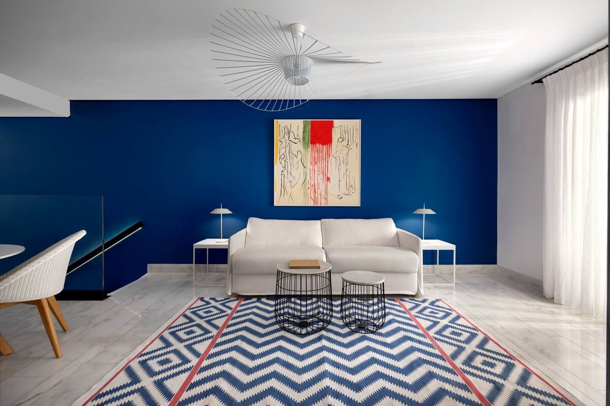 A modern living room with a blue accent wall, white sofa, two side tables, and a geometric patterned rug.
