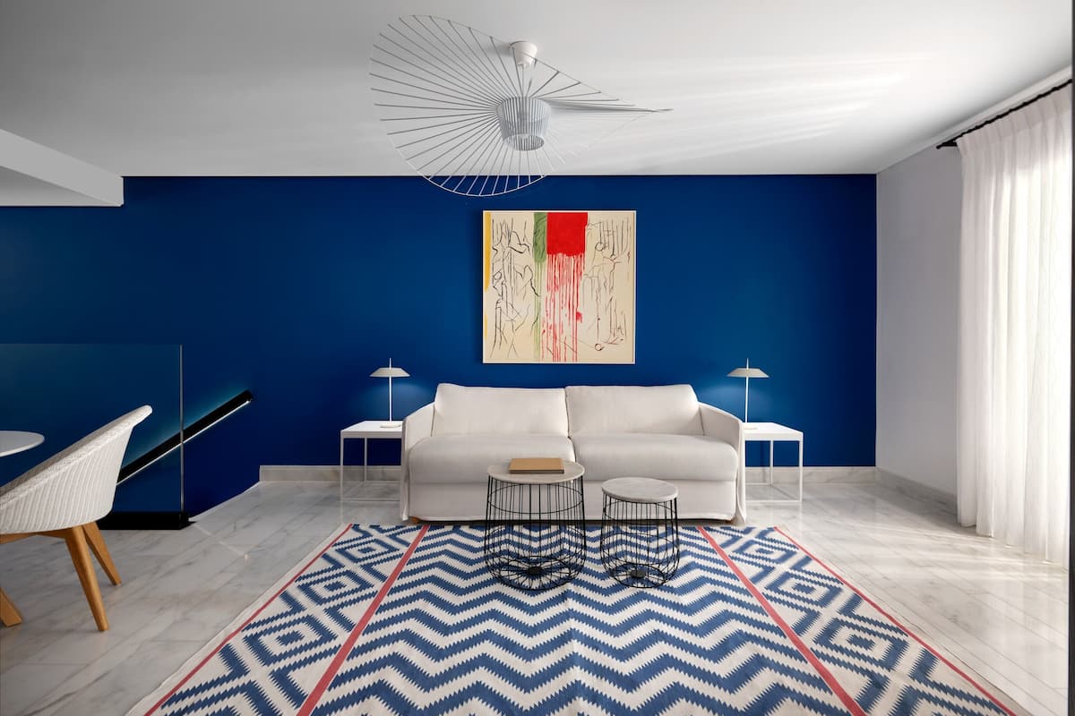 A modern living room with a blue accent wall, white sofa, two side tables, and a geometric patterned rug.
