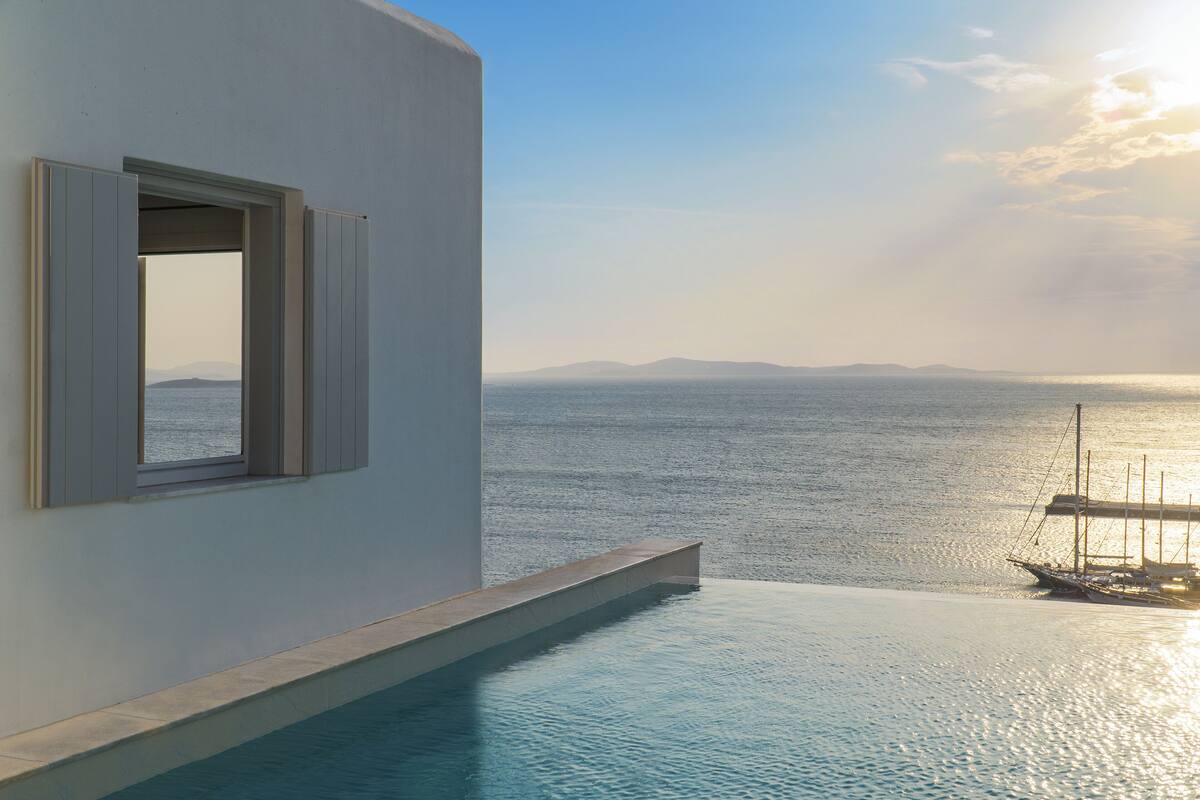A modern building with a pool extending to the sea, a clear view of the water, and a distant landmass.