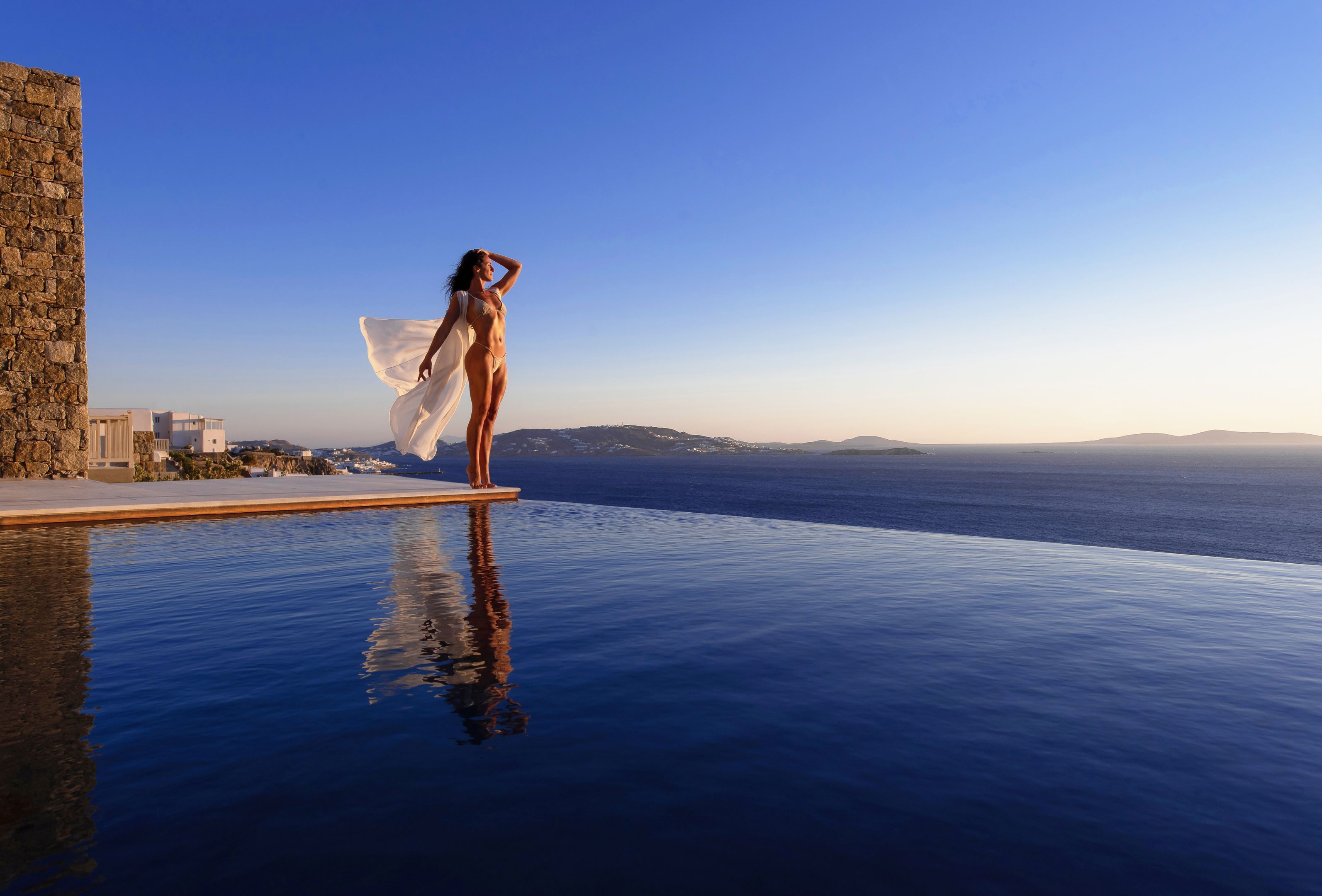 Una persona in piedi sul bordo di una piscina, con vista sul mare e sugli edifici sullo sfondo.
