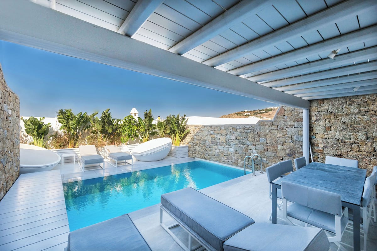 A modern outdoor pool area with a stone wall, lounge chairs, and a table.