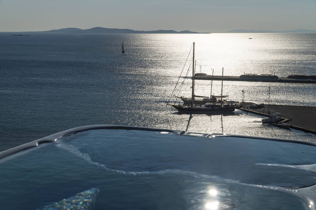 A marina with boats docked, a clear view of the sea, and distant mountains.