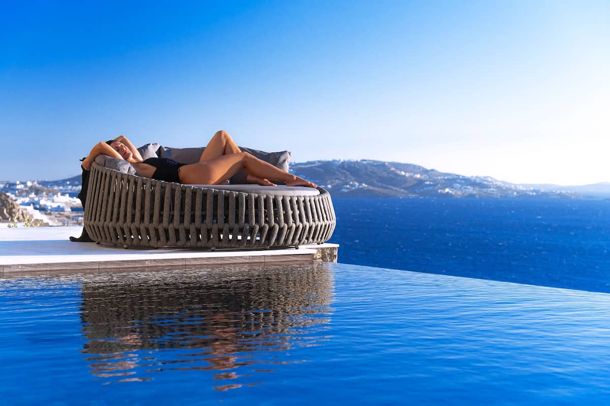 A circular wicker lounge chair by a pool with a clear view of the sea and distant mountains.