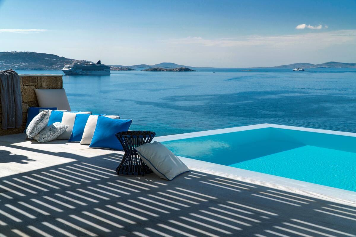A poolside area with a view of the sea, a ship, and distant hills.