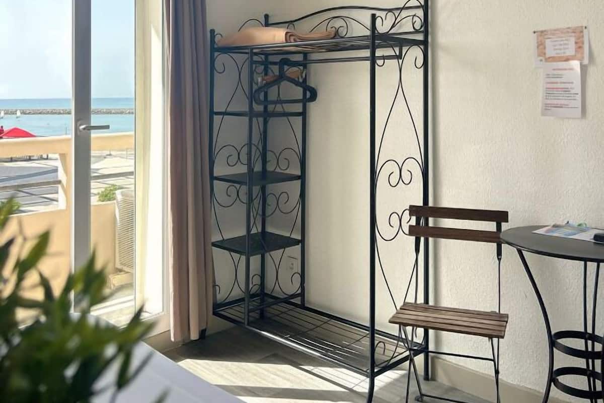 A room with a bunk bed, a desk, a chair, a TV, and a view of the beach.