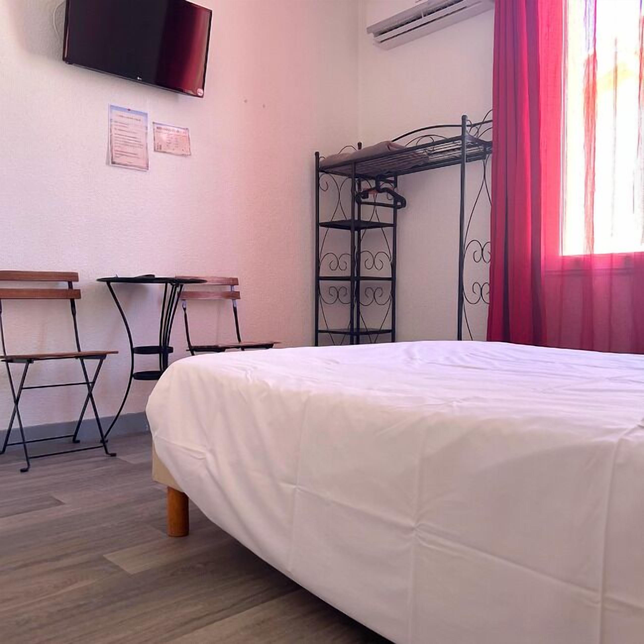 A room with a bed, two desks, a TV, and a window with curtains.