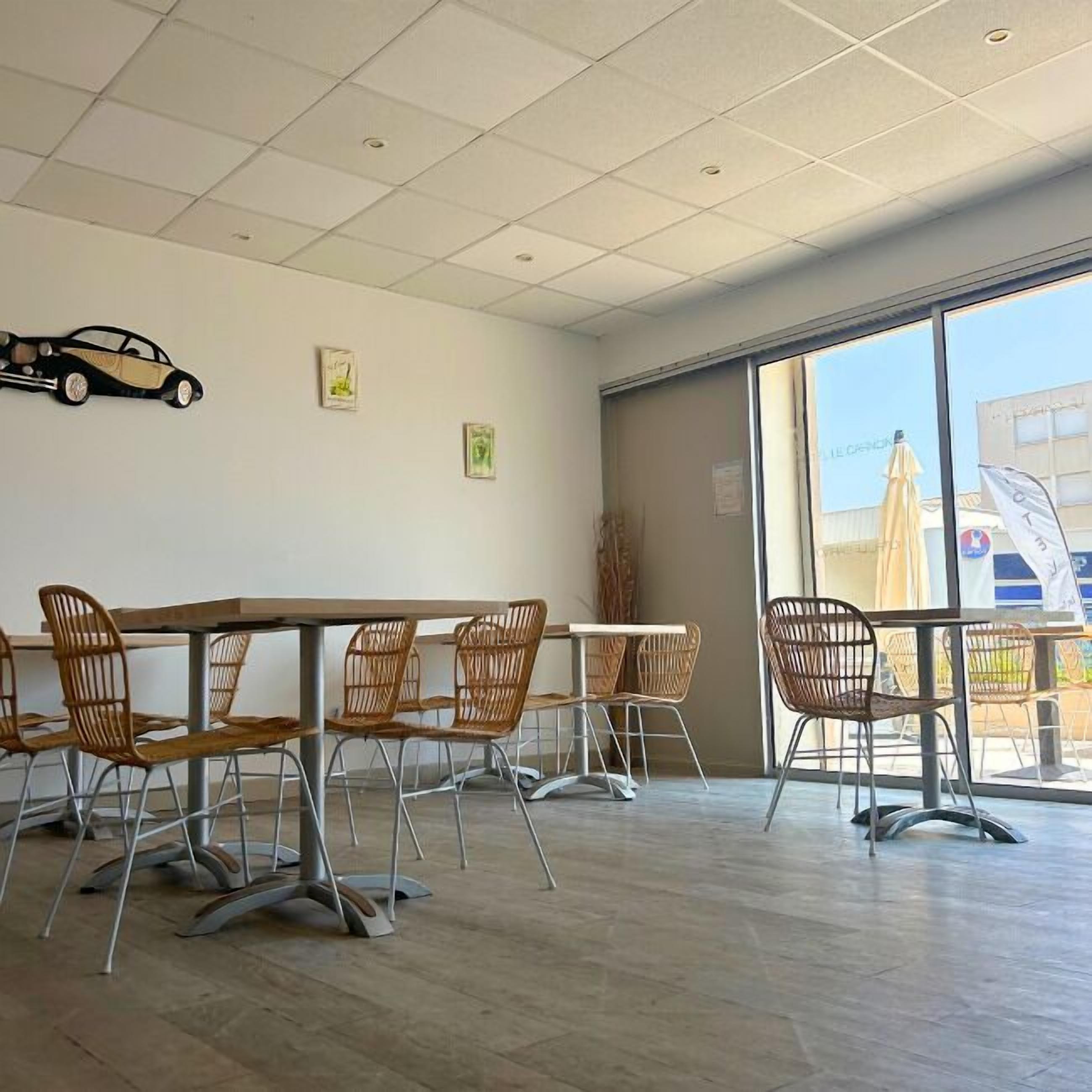 Un comedor con un ventanal grande, una decoración con forma de coche en la pared y sillas de mimbre.