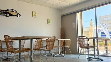A dining area with a large window, a car-shaped decoration on the wall, and wicker chairs.