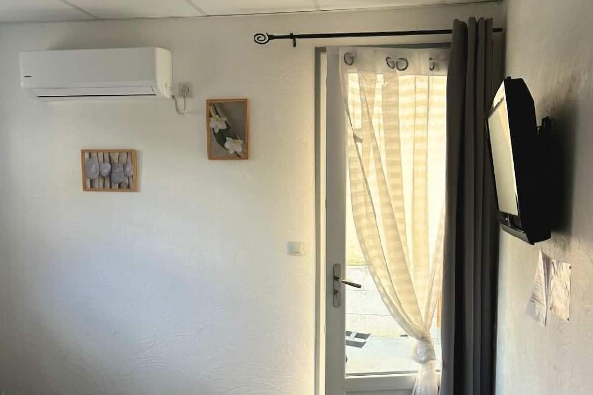 A bedroom with a bed, an air conditioning unit, a door with curtains, and a small window.