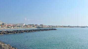Vista sulla costa con un molo roccioso, mare calmo e edifici sullo sfondo.