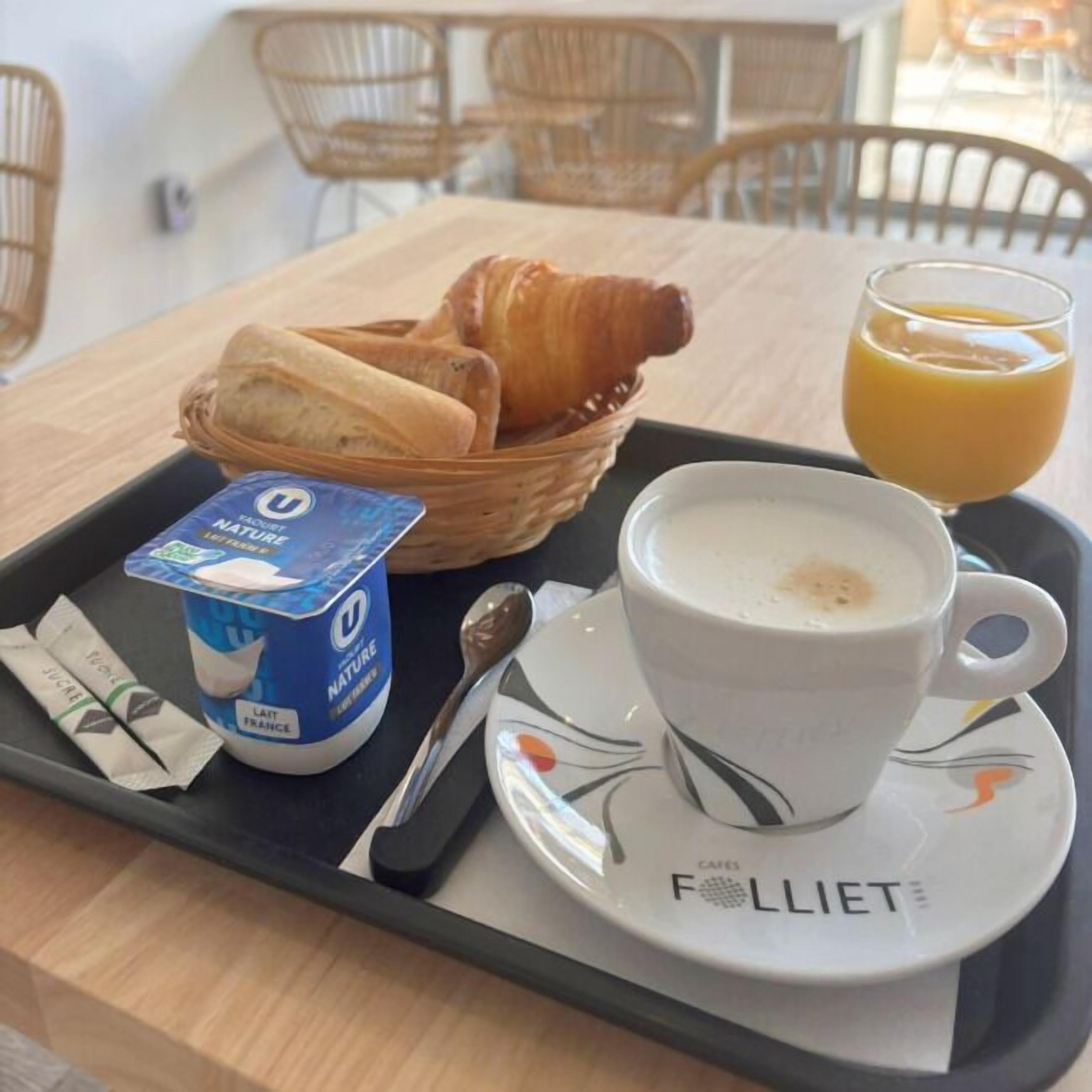 A breakfast tray with croissants, a cup of coffee, a glass of orange juice, and a packet of yogurt.
