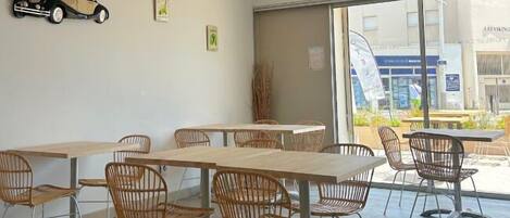 A modern interior with wooden tables and wicker chairs, large windows, and a car decoration on the wall.