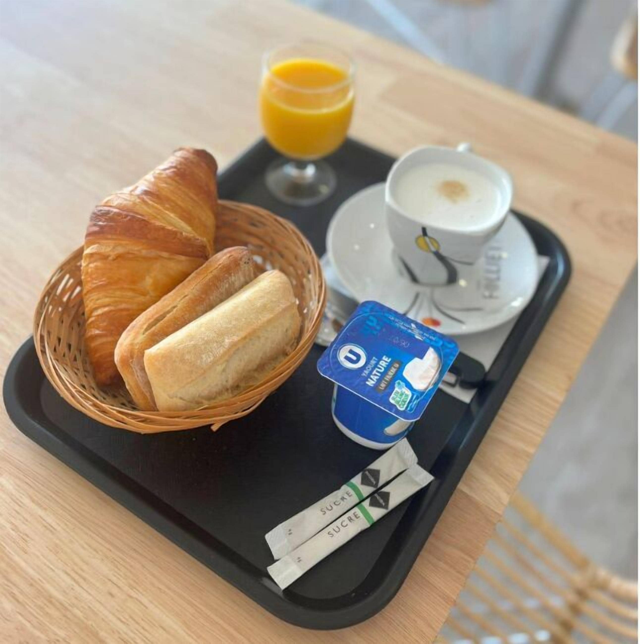 A breakfast tray with croissants, a glass of orange juice, a cup of coffee, and a container of yogurt.