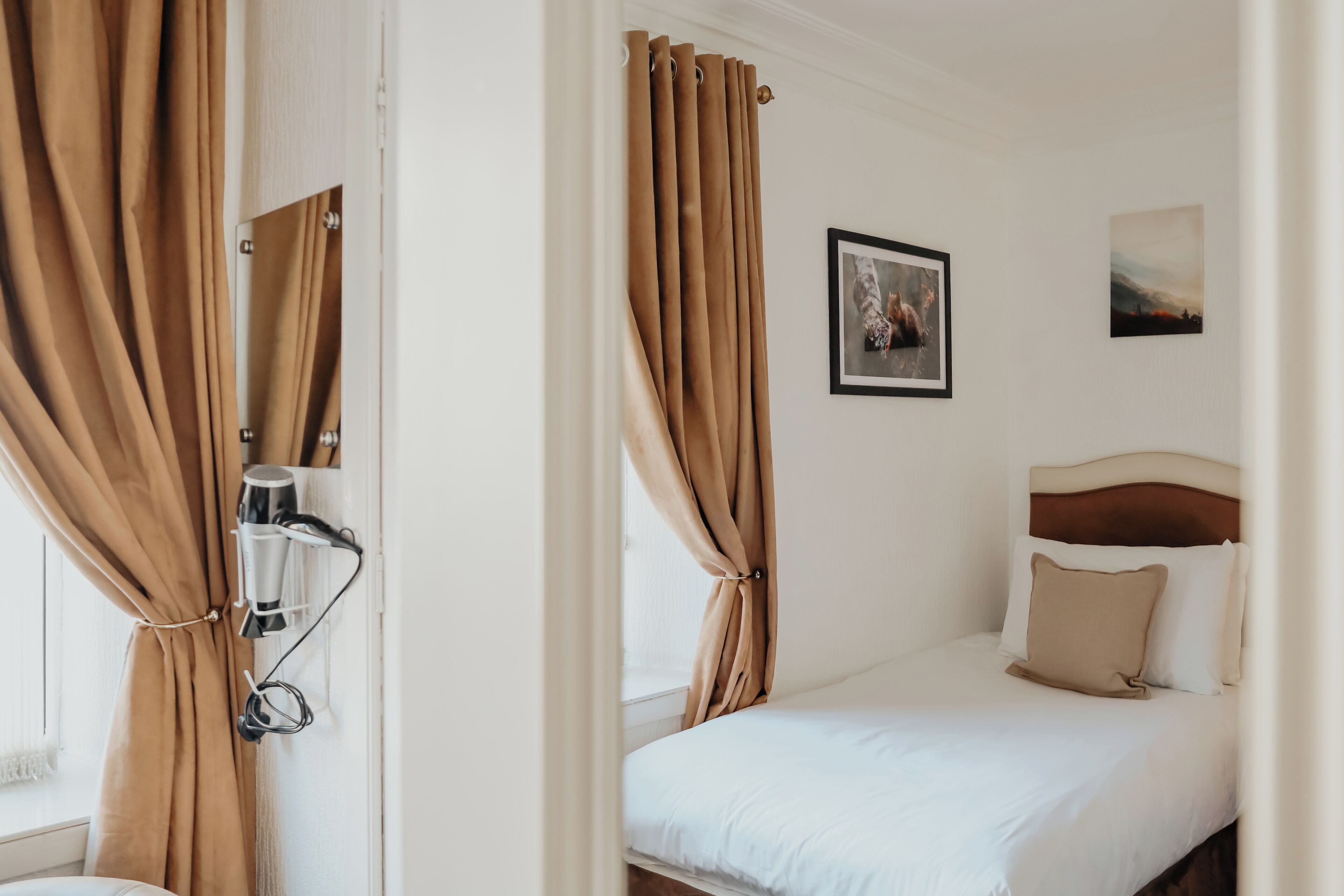 A hotel room with a bed, curtains, a headboard, a wall-mounted heater, and a framed picture.
