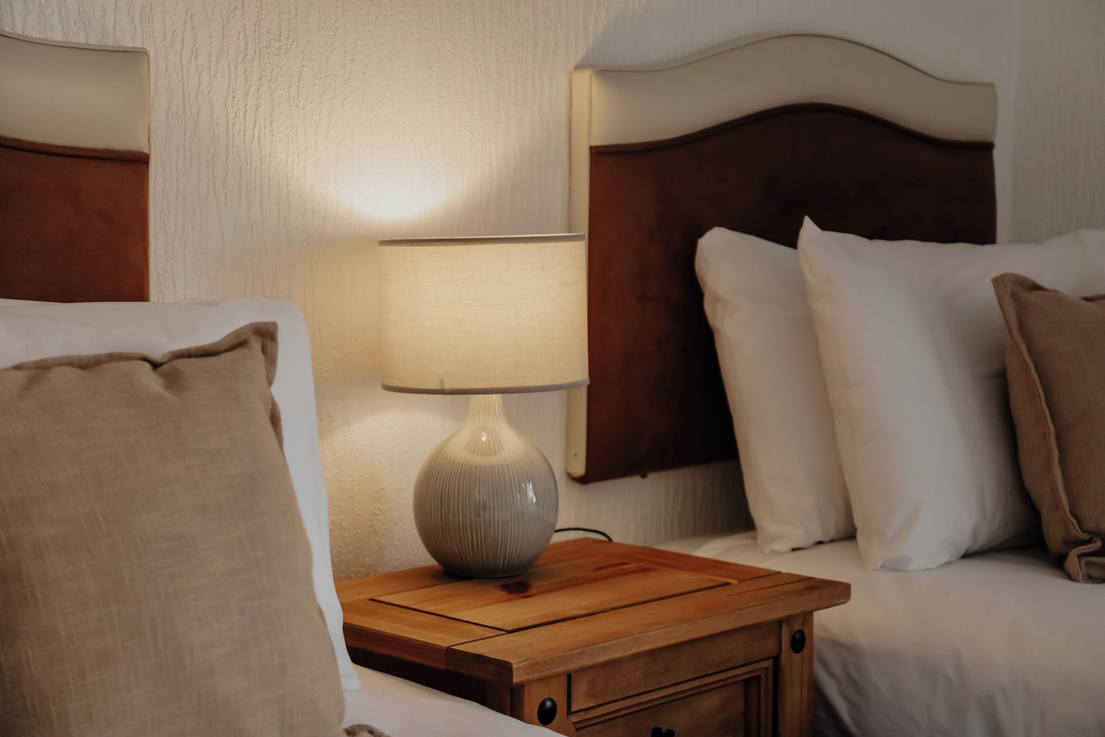 A neatly made bed with white bedding and a wooden nightstand with a lamp.