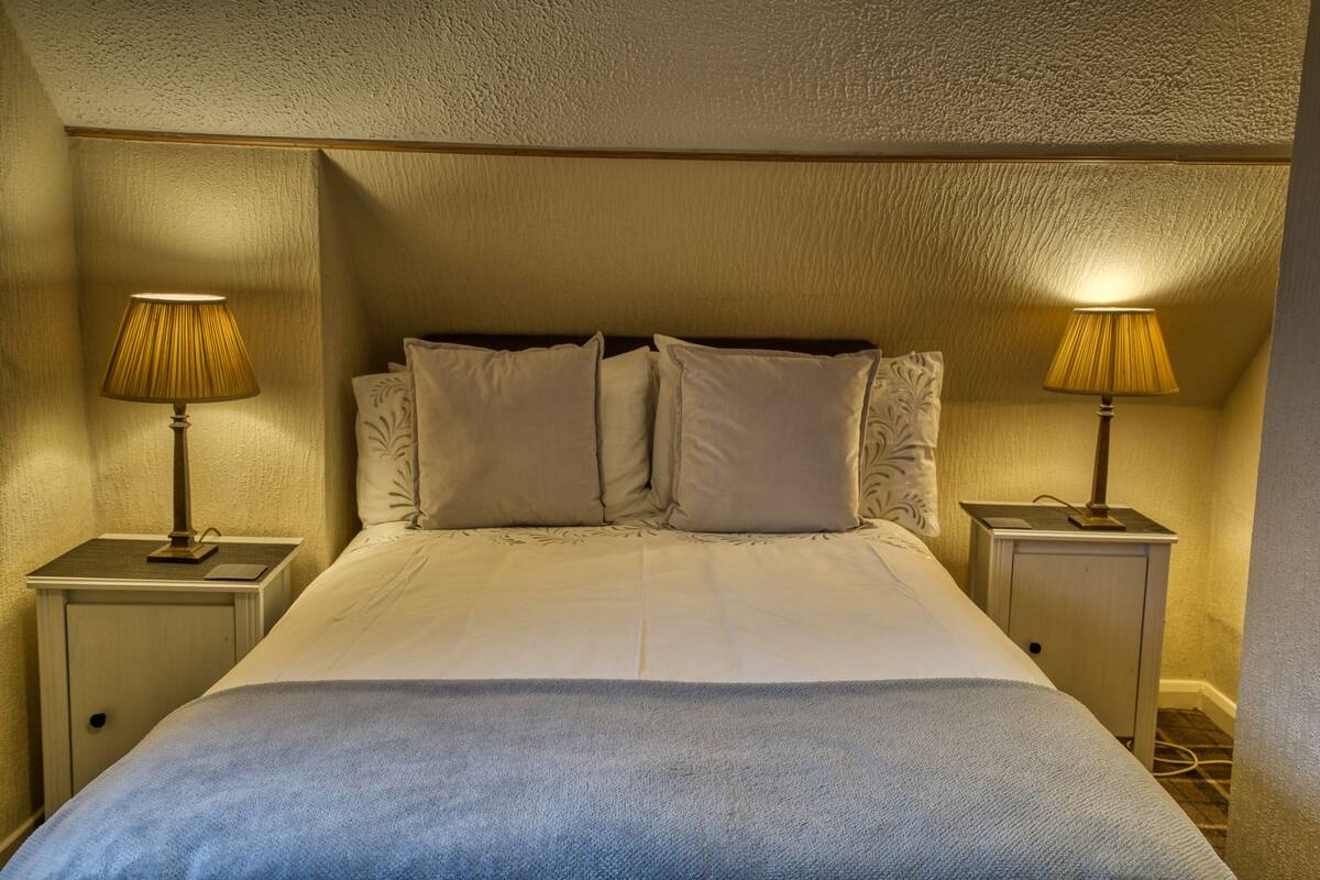 A neatly made bed with a blue blanket, two bedside lamps, and a headboard.