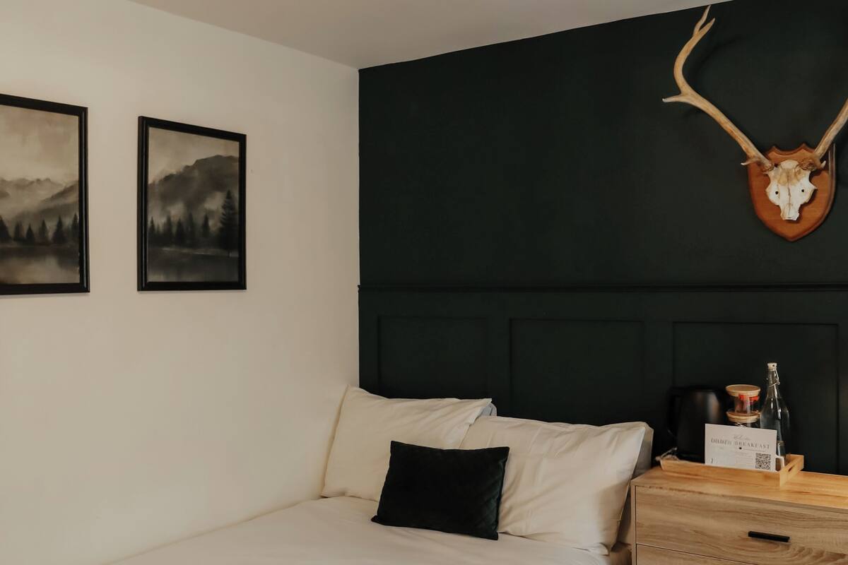 A bedroom with a bed, a dresser, wall-mounted lights, and two framed pictures.