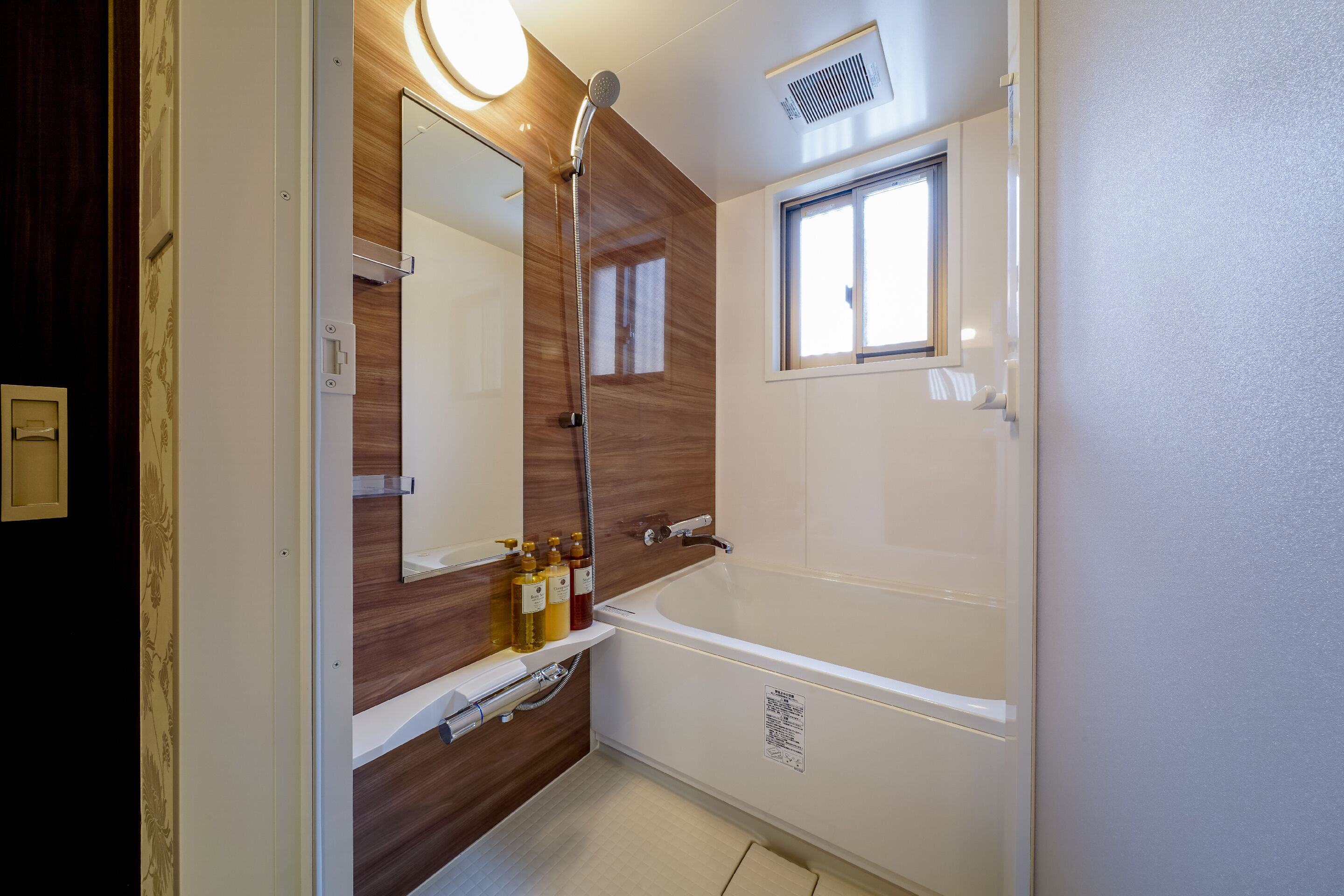 A modern bathroom with a bathtub, a large mirror, and a window.