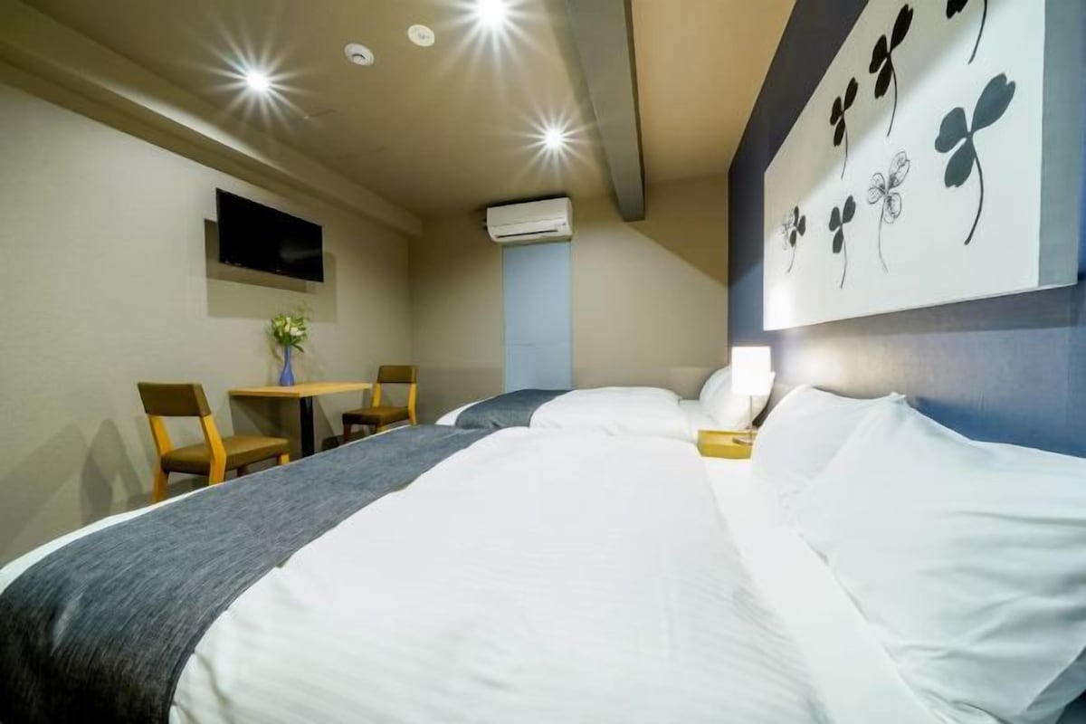 Ett hotellrum med en stor säng, ett skrivbord med en stol, en tv som är monterad på väggen och en luftkonditioneringsanläggning.