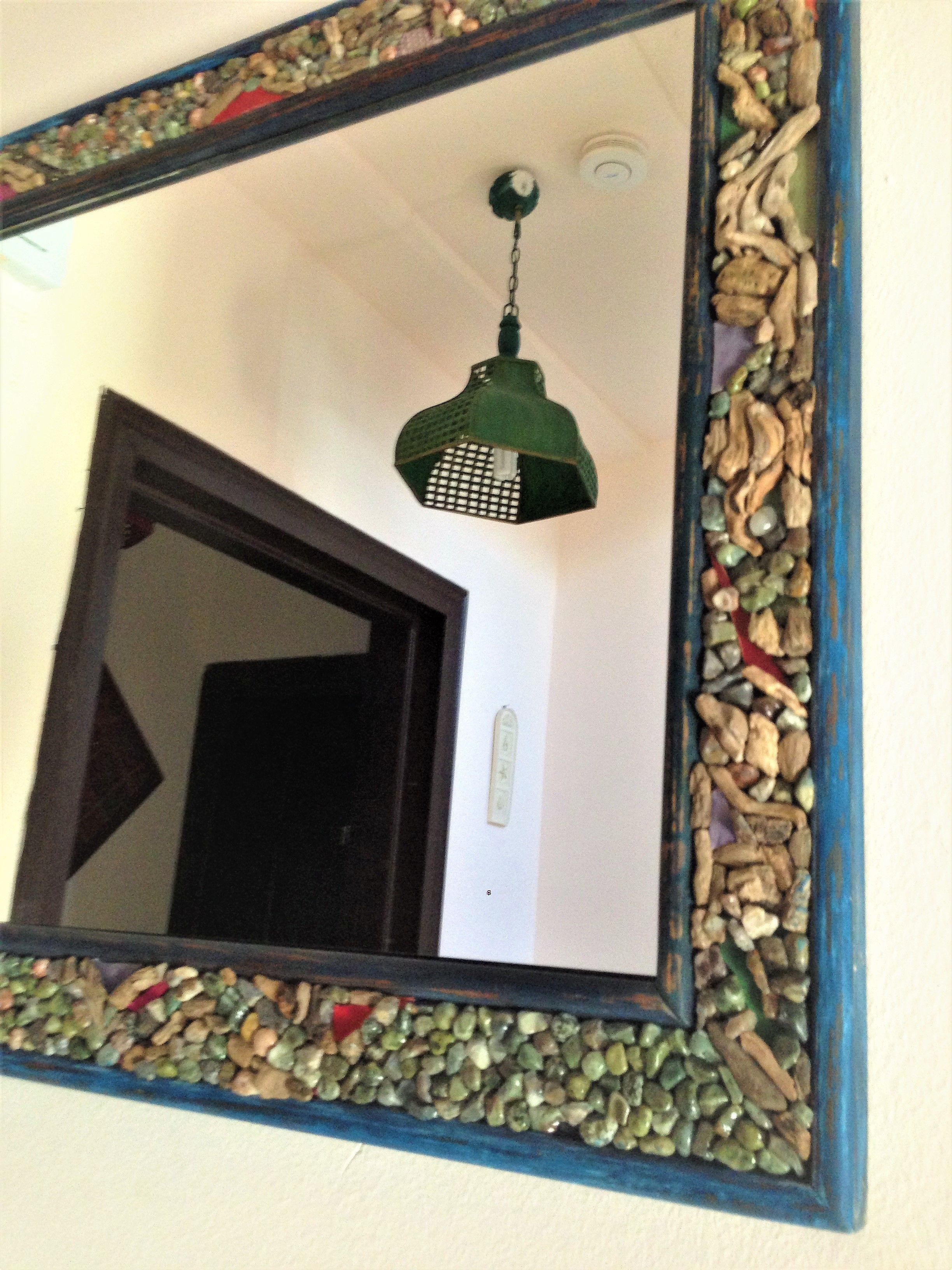 Espelho com moldura decorativa com pedras e luminária pendente verde.