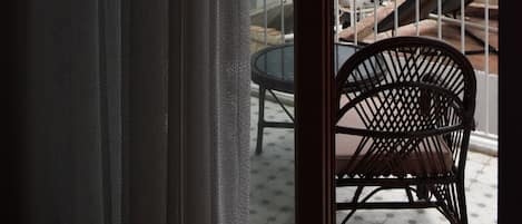 A balcony with a view of the sea and mountains, a chair, and a table.