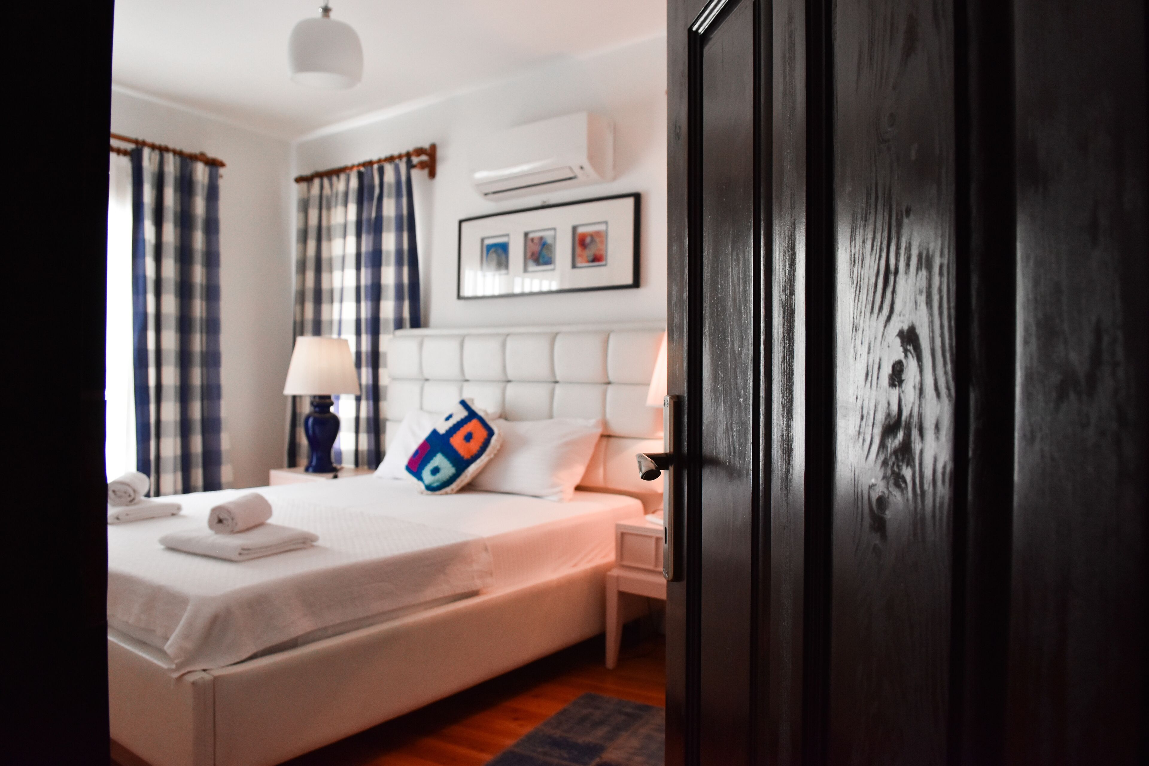 Una habitación de hotel con cama, mesita de noche, lámpara, aire acondicionado instalado en la pared y una puerta.