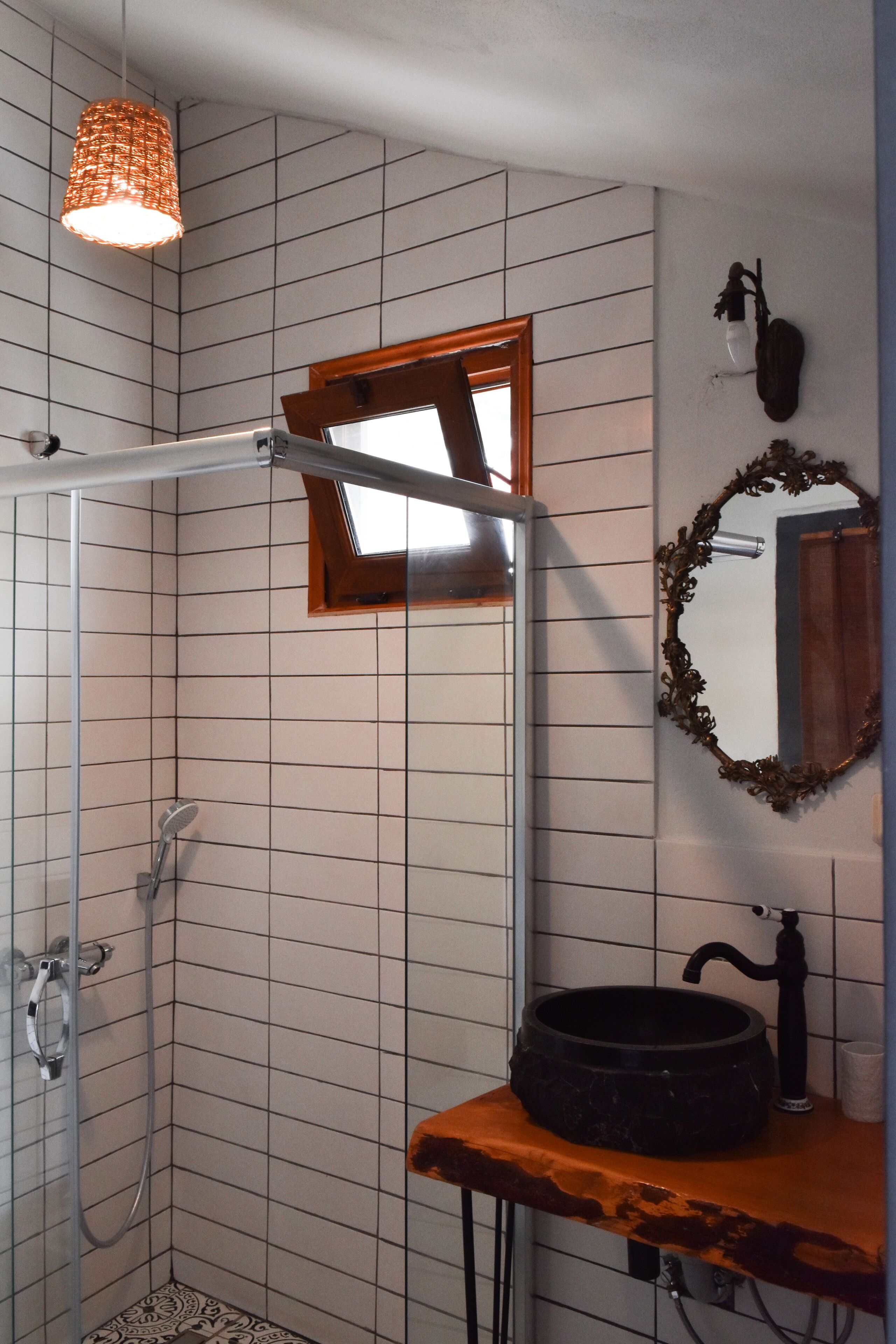 Een badkamer met een douche, een wastafel met een rond bassin, een spiegel met een sierlijk frame en een hanglamp.