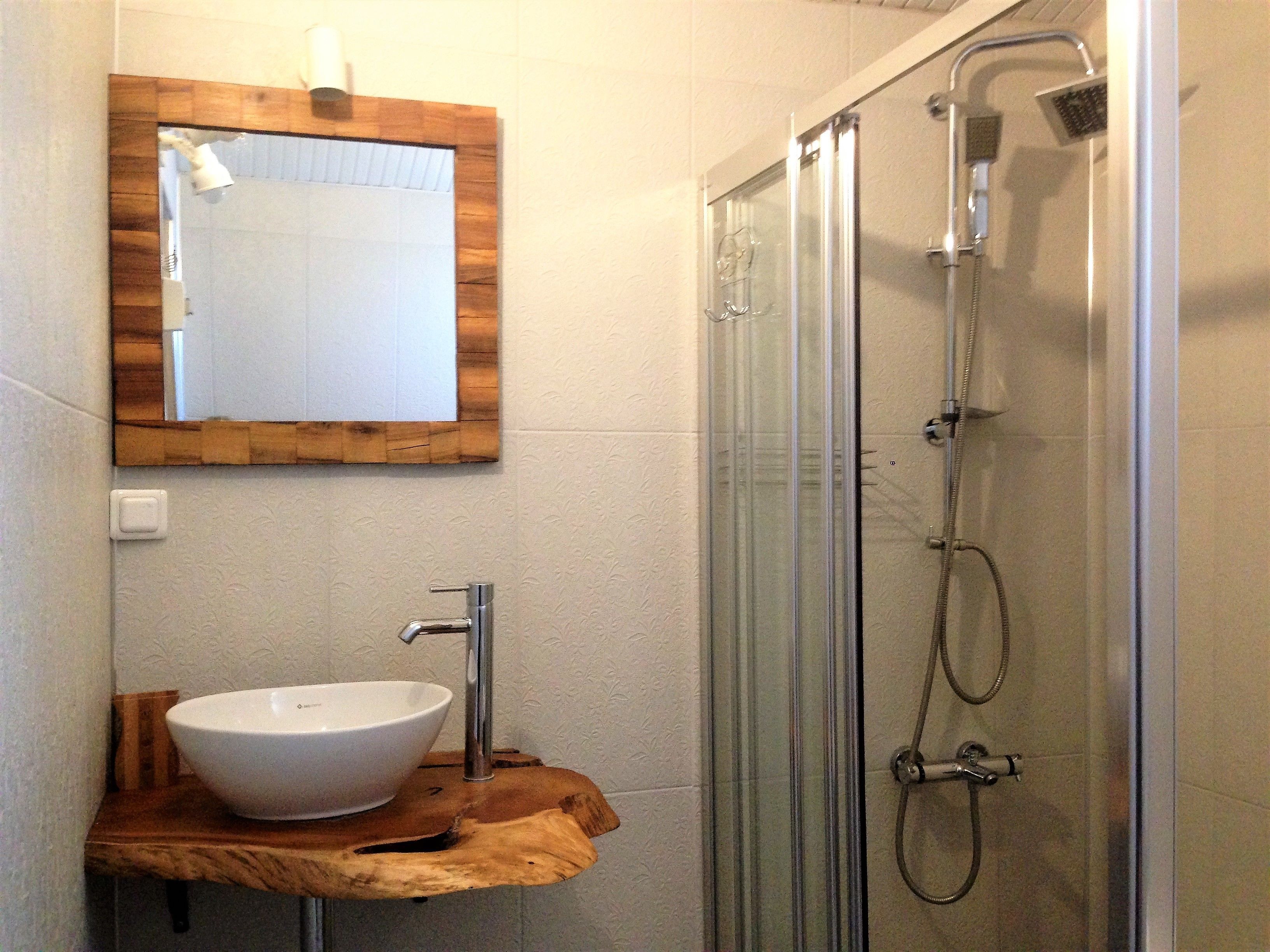 A bathroom with a wooden vanity, a white sink, a mirror, and a glass-enclosed shower.
